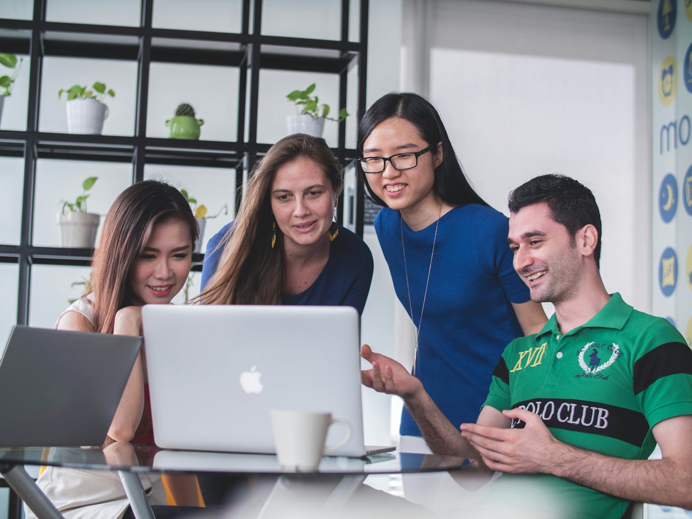 Four people gathered around a laptop in a bright office